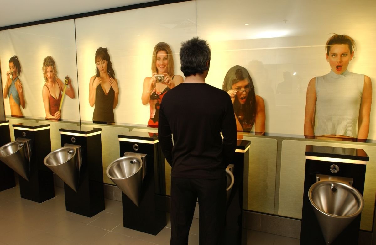 Urinarios con un mural detrás con fotos de mujeres mirando hacia abajo y gesticulando